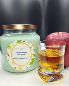 A glass of bourbon sits in front of a red apple and a large 16 oz Apothecary Jar Candle - Lavender. The background is dark with a reflective surface.