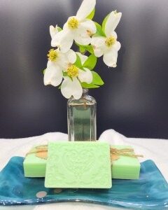 A 16 oz Apothecary Jar Candle in Lavender stands behind two mint green embossed soap bars, which sit on a blue ceramic tray against a dark background.