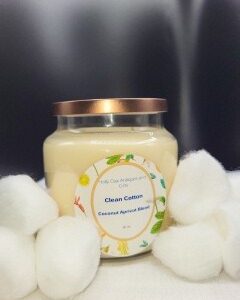 A 16 oz Apothecary Jar Candle labeled Lavender with a copper lid is surrounded by several white cotton balls, set against a dark, blurred background.