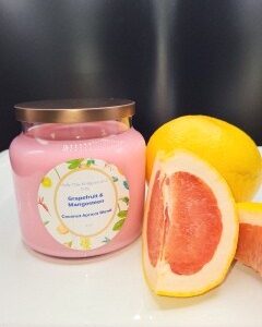 A 16 oz Apothecary Jar Candle labeled Lavender sits on a white surface with a dark background, next to a halved grapefruit and a whole grapefruit.