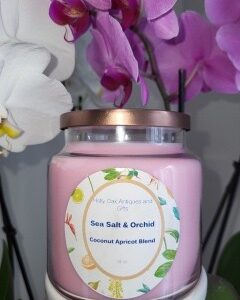 A 16 oz Apothecary Jar Candle - Lavender in a glass jar is set in front of blooming white and purple orchids.