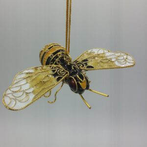 A decorative bee ornament with gold and black detailing, translucent filigree wings, and a hanging gold string against a plain light background.