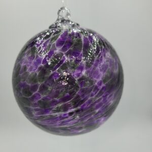 A round glass ornament with a swirl pattern in shades of purple and white, hanging against a plain, light gray background.