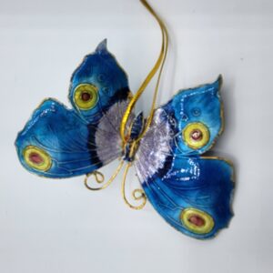 A decorative blue butterfly ornament with yellow and red eye spots on its wings, gold wire antennae, and a gold hanging string, against a plain white background.