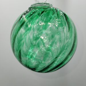 A round glass ornament with green and white swirled patterns hangs against a plain white background. The ornament has a small clear loop at the top for hanging.