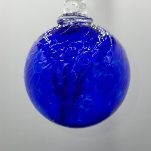 A round, hand-blown glass ornament in vibrant cobalt blue, featuring swirling patterns and a small clear loop at the top for hanging, set against a plain white background.