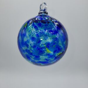 A round glass ornament with swirling blue and green patterns hangs against a plain, light gray background. The ornament is glossy and semi-transparent, resembling the appearance of Earth.