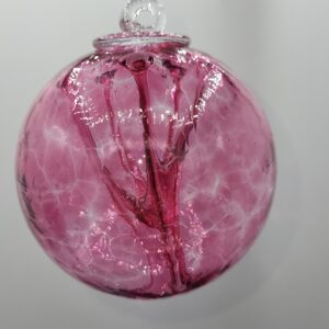 A round, transparent glass ornament with swirling pink and purple patterns inside, hanging against a plain white background.
