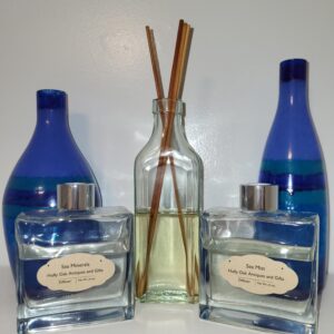 Two blue decorative vases flank a glass reed diffuser bottle with brown sticks, placed between two square glass bottles labeled Sea Minerals and Sea Mist on a white surface against a light background.