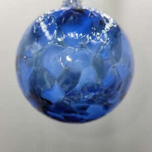 A close-up of a blue glass ornament with a textured, mosaic-like surface, hanging against a blurred, light-colored background.
