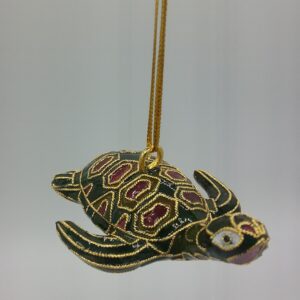 A decorative turtle ornament with detailed gold, green, and red patterns hangs from a gold string against a plain light background.