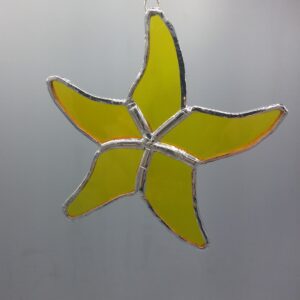 A yellow, five-pointed stained glass star ornament outlined in silver hangs against a plain gray background.