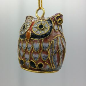 A small, decorative owl ornament with gold outlining and details hangs from a gold string against a plain, light background. The owl features intricate patterns in brown, black, and gold.