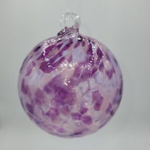 A glass ornament with a loop at the top, featuring a mosaic pattern in shades of purple, pink, and white, hanging against a plain light background.