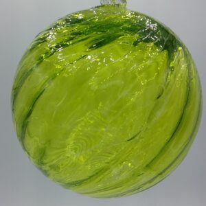 A round, hand-blown glass ornament with swirls of yellow and green, featuring a small clear glass loop at the top for hanging, set against a plain light background.