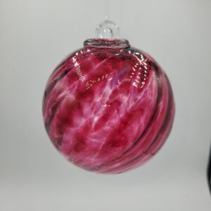 A round glass ornament with swirling patterns of pink and white, hanging by a clear string against a plain, light background.