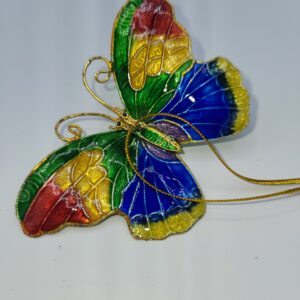 A decorative butterfly with vibrant red, green, yellow, and blue wings, outlined in gold, against a plain white background. Gold wire details accent the body and wings, with a gold string attached.