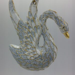 A glass swan ornament hangs from a gold string, featuring white and blue coloring with gold glitter accents outlining its wings and body, against a plain light background.