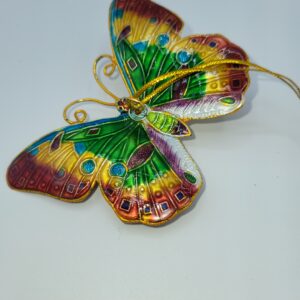 A colorful butterfly ornament with green, yellow, red, and blue patterns on its wings, attached to a gold hanging string, displayed on a plain white background.