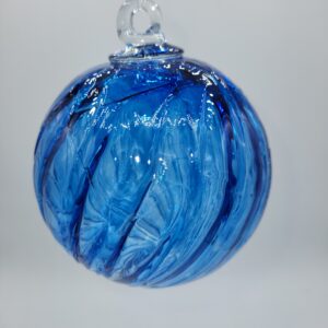 A close-up of a blue glass ornament with swirling patterns, hanging by a clear loop against a plain white background.