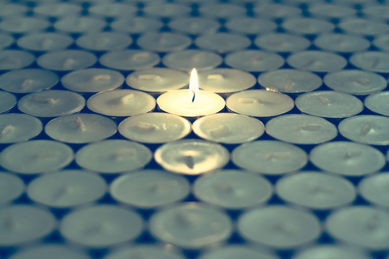 A single tealight candle burning brightly amidst a sea of unlit candles, creating a serene focus. Learn about Phthalates in Candles